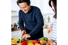 Man and woman cooking with vegetables in a kitchen.
